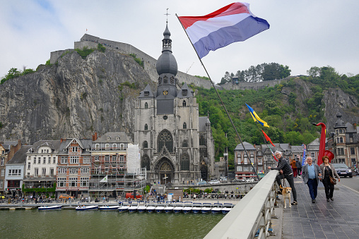 Charles de Gaulle Bridge over the Meuse with Dutch flag and view of the Collegiale Ou Lady church near the citadel in Dinant, Wallonia, Belgium