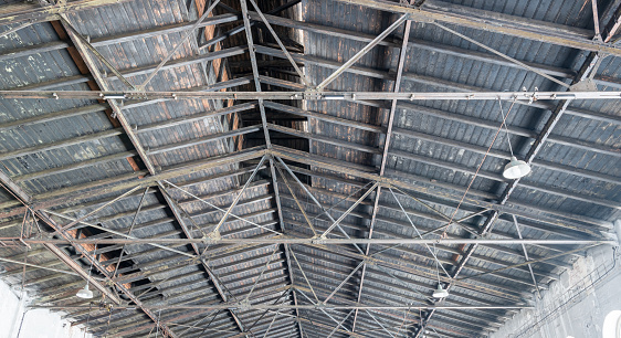 Gable roof truss of a large, vintage factory hall. Roofing construction (sheathing) made of wooden planks. Industrial interior.