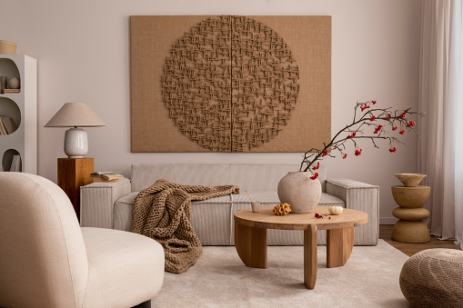 Creative composition of living room interior with mock up poster frame, beige sofa, wooden coffee table, rounded shapes armchair, vase with rowanberry and personal accessories. Home decor. Template.