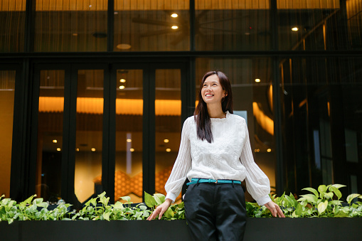 Portrait of Asian businesswoman leaning at garden outside of office building