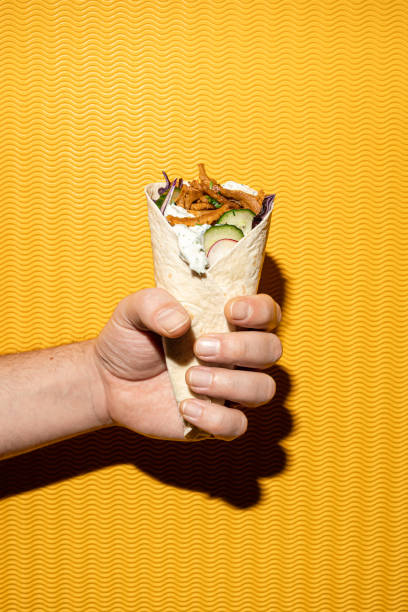 Close-up of a fastfood pita gyros sandwich held by a male hand, yellow background Close-up of a fastfood pita gyros sandwich held by a male hand, yellow background, flash pita bread isolated stock pictures, royalty-free photos & images