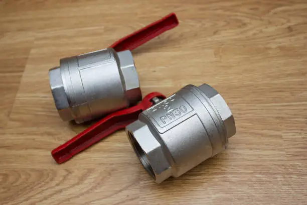 Photo of Two large two-inch ball valves with a red lever handle lie on the table