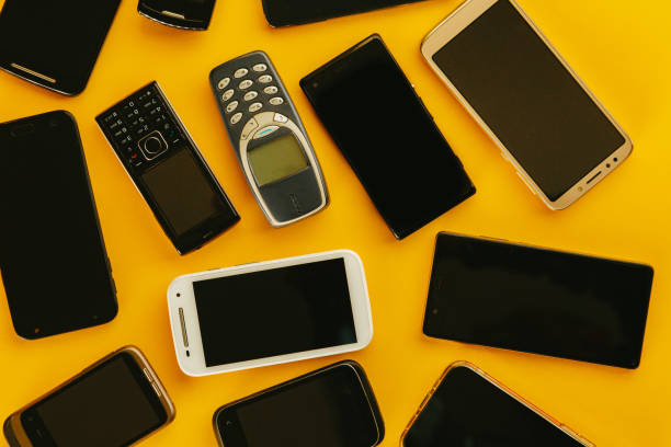 Flat lay depicting multiple generations of cell phone handsets on a yellow background.