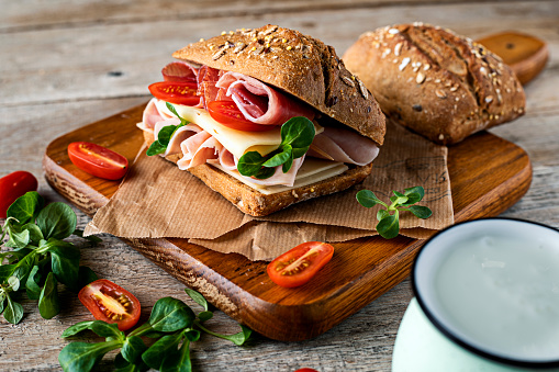 Two fresh submarine sandwiches with ham, cheese, bacon, tomatoes, lettuce, cucumbers and onions on dark wooden background