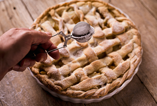 Homemade apple pie on wooden rustic background. Close-up shot of a human hand sprinkling sugar on a pie