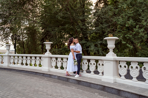 A passionate sexual kiss in the park against the backdrop of summer greenery. Young white American couple kisses against the backdrop of trees and stairs fence in summer park. Selective focus