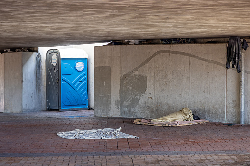 Cape Town, South Africa - December 13th 2022: Homeless man sleeping under a bridge beside a public toilet