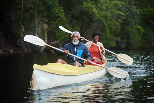 Mature couple laughing while paddling a double canoe together down a river during a weekend getaway in nature