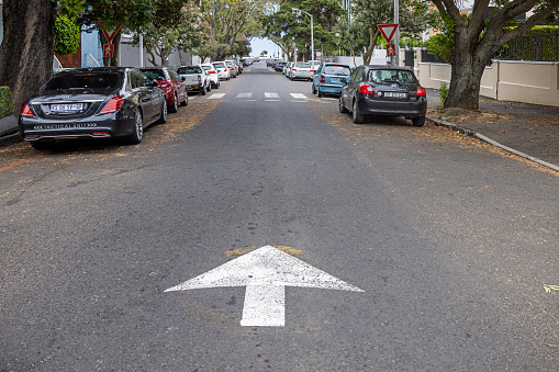 Cape Town, South Africa - December 11th 2022: Arrow pointing down a one way residential street with parked cars and lined with trees