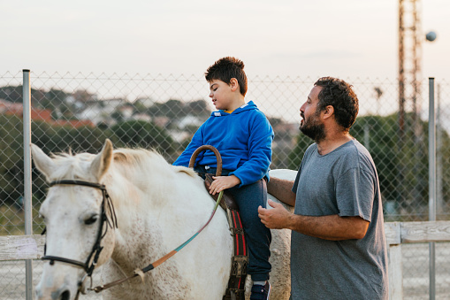 Outdoor and rural scene of a boy with cerebral palsy riding a horse next to instructor