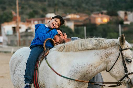 Boy with cerebral palsy hugging his physiotherapist during equine therapy session with a horse