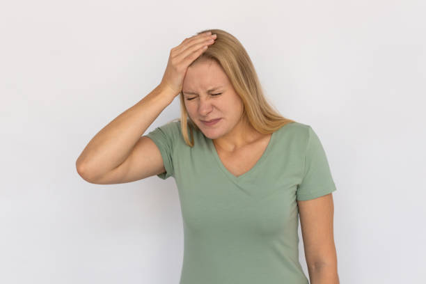 Stressed young woman with hand on forehead Stressed young woman with hand on forehead. Portrait of frustrated Caucasian female model with fair hair in green T-shirt with closed eyes realizing mistake. Regret, stress, headache concept regrets stock pictures, royalty-free photos & images