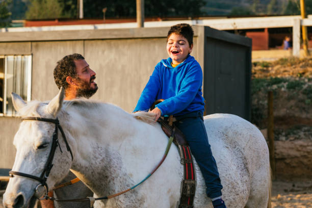 happy boy with cerebral palsy riding a horse during equine therapy - teaching child horseback riding horse imagens e fotografias de stock