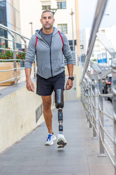 Full body mature sportsman with prosthetic leg walking on slope outside modern building after fitness training in city
