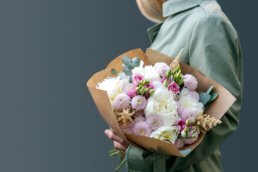 A woman holds a bouquet of peonies against a gray background. Pastel colors. Spring tones.