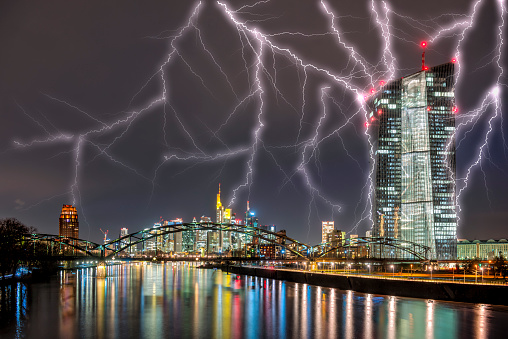 The ECB (European Central Bank) in Frankfurt am Main in the evening with artificial lighting and the skyline in the background with striking thunderbolts