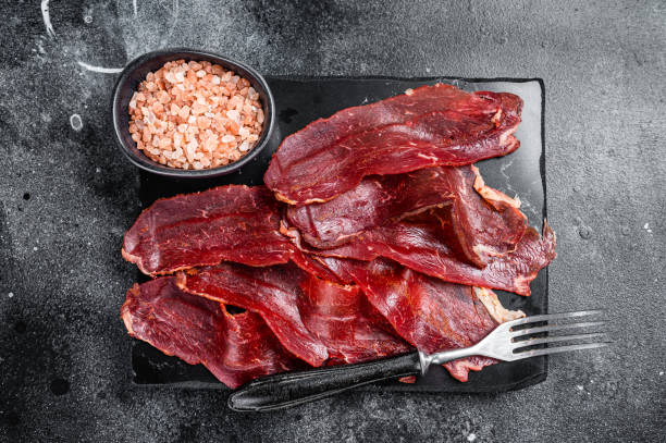 istock Turkish sliced pastrami (kayseri pastirma), dried beef meat with spices on marble board. Black background. Top view 1459619635