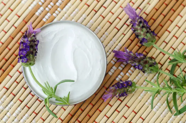 Photo of White facial mask (face cream, hair treatment, body butter) in a small jar and lavender flowers. Natural skin and hair care concept. Top view, copy space.