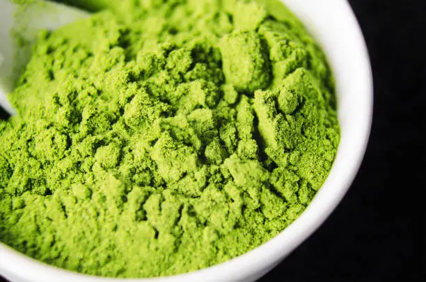 Photo of Matcha green tea powder in a white bowl, close-up. Selective focus