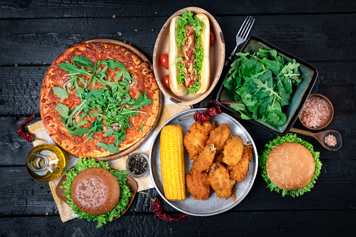 Pizza, hamburgers, fried chicken and hot dog. Top view on a dark wood background.