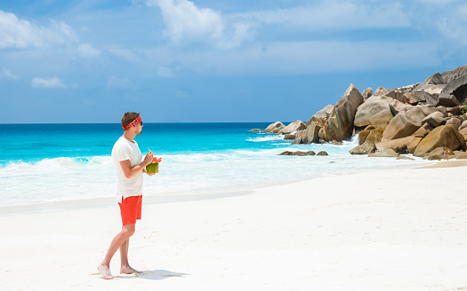 Young men in swim short with a coconut drink on a tropical beach La Digue Seychelles Islands.