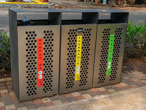 Jakarta, Indonesia - August 19, 2022: Three metal garbage bins at a city park with each colored classifications and words saying B3 Garbage, Anorganic, and Organic.