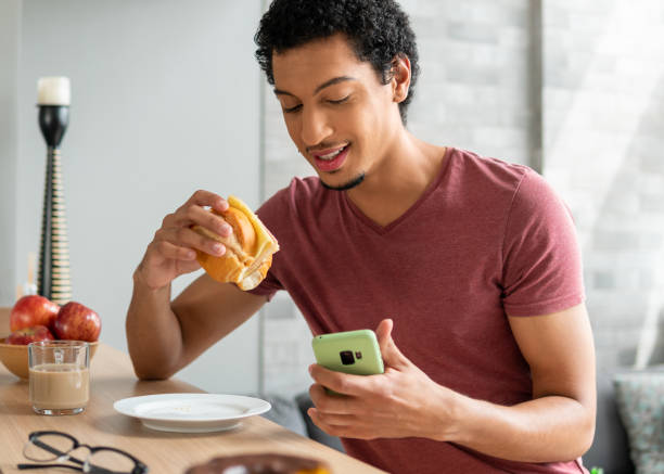 l’homme prend son petit-déjeuner et regarde son téléphone portable - bagel coffee morning breakfast photos et images de collection