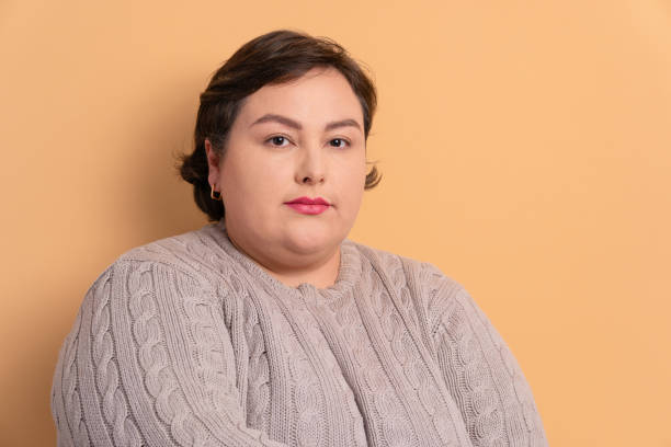 mujer seria mirando a la cámara en fondo beige. - pelo corto para gorditas fotografías e imágenes de stock