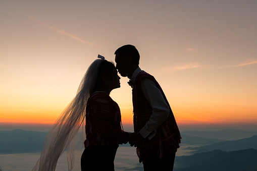 silhouette of wedding Couple in love kissing and holding hand together during sunrise with morning sky background