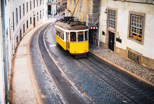 A high angle view of a traditional yellow tram on a sloping street in Lisbon, Portugal.