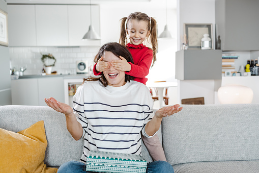 Beautiful pregnant woman enjoying with her cute little daughter at home. A little girl covers her mother's eyes