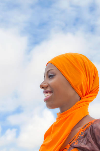 menina bonita (18 anos) vestindo um lenço de cabeça tradicional e um vestido bordado, cor laranja, ao ar livre, céu azul, paisagem das nuvens, foto, formato horizontal - hijab profile teenager islam - fotografias e filmes do acervo