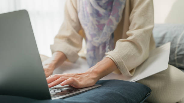 istock Closeup young muslim woman sit on bed with computer laptop and on folding laptop table, portable holder stand hold paperwork and think create on work idea in bedroom at home. Work from home. 1459639152