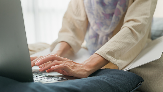 Closeup young muslim woman sit on bed with computer laptop and on folding laptop table, portable holder stand hold paperwork and think create on work idea in bedroom at home. Work from home concept.