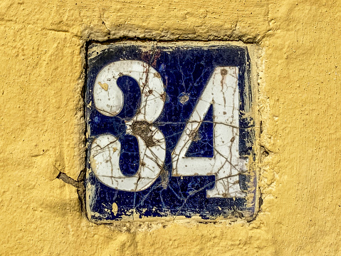 Close-up view of weathered tile with the number 34 in yellow wall