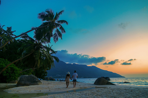 A couple of men and women watching the sunset o a tropical beach at the Seychelles Islands.