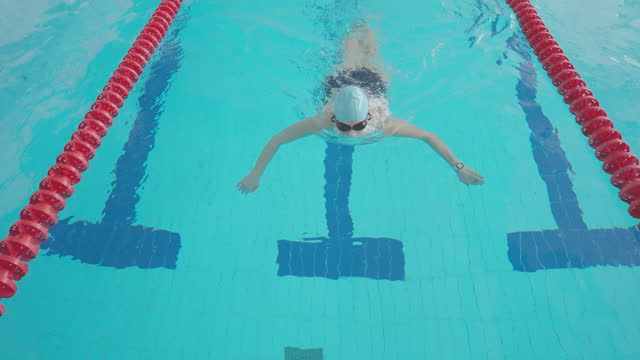Middle-aged woman swimmer swims in breaststroke style.