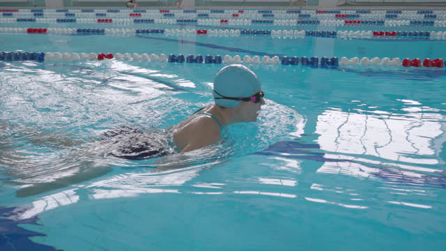 Middle-aged woman swimmer swims in breaststroke style.