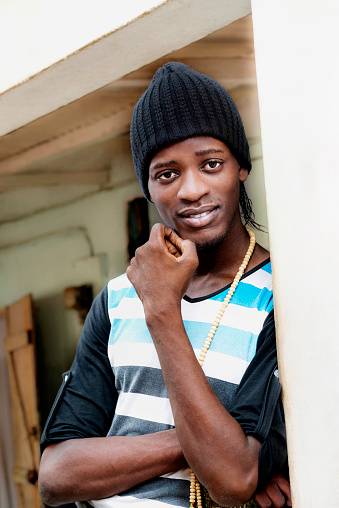 Young African Muslim man standing on a porch and wearing a black woolen cap, a rosary around his neck, photo