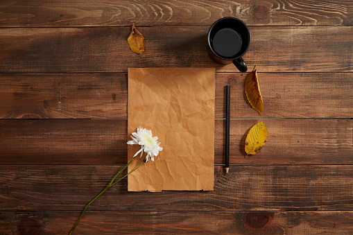 Pencil and blank paper wooden background with cup of coffee, daisy bunch and autumn leaves.