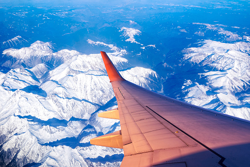 Airplane flying above mountains peaks covered by snow in winter