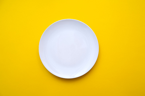 White empty plate with blank surface on bright yellow backdrop, top view