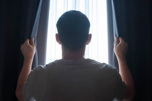 istock Man stands at window and opens curtains rear view. 1459661474