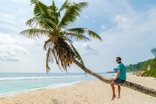 Young men relaxing at a palm tree on a tropical white beach at the La Digue Seychelles Islands.