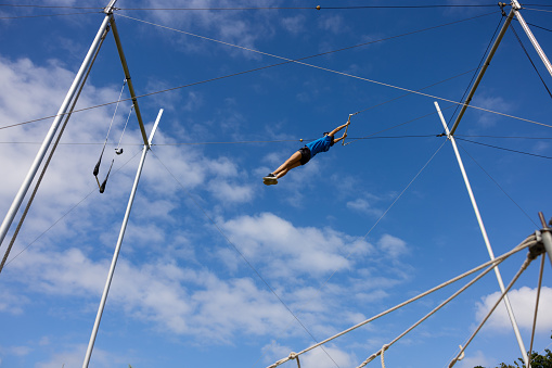 Female trapeze artist flying in the blue sky