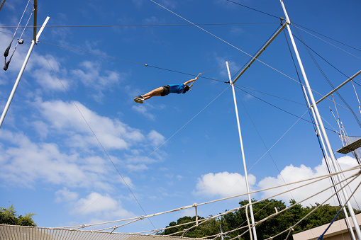 Female trapeze artist flying in the blue sky
