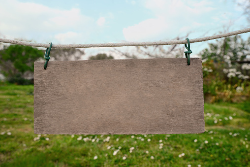 Blank wooden board hanging on rope in countryside. Space for text