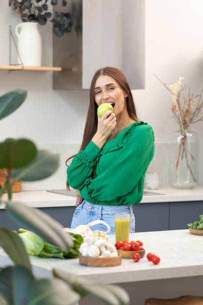 istock An attractive brunette holds a green apple while standing at the kitchen table. 1459671466