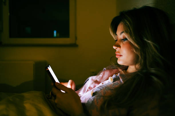 istock Young caucasian woman using smartphone, lying on a bed at home in the evening. 1459672187