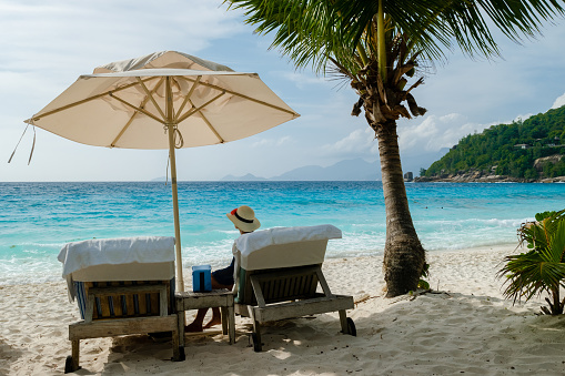 women relaxing in a Beach chair at a tropical beach sunbed chair and umbrella and palm trees in Mahe Seychelles.
